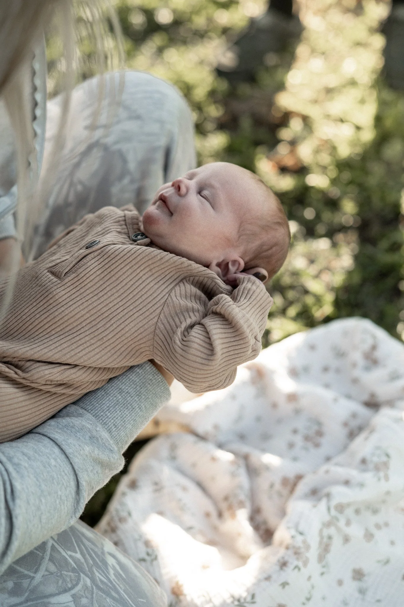 A baby with a pacifier sleeping in someone's arms outdoors in snowy landscape with trees.