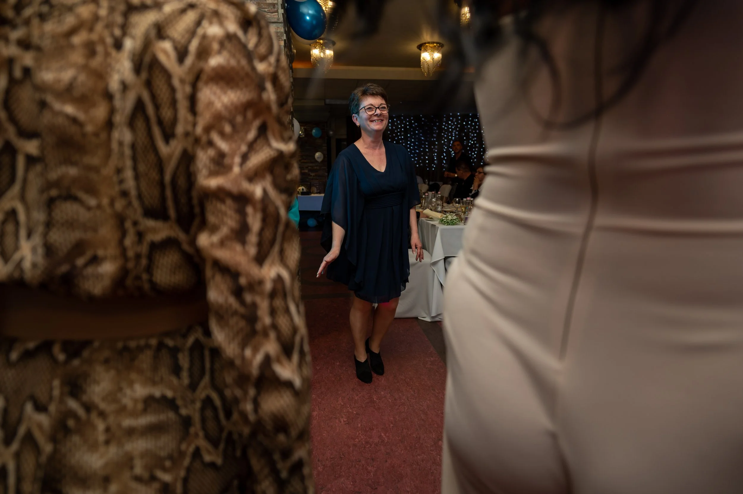Black and white photo of a woman with long wavy hair, smiling, wearing a pearl necklace and an off-the-shoulder dress.