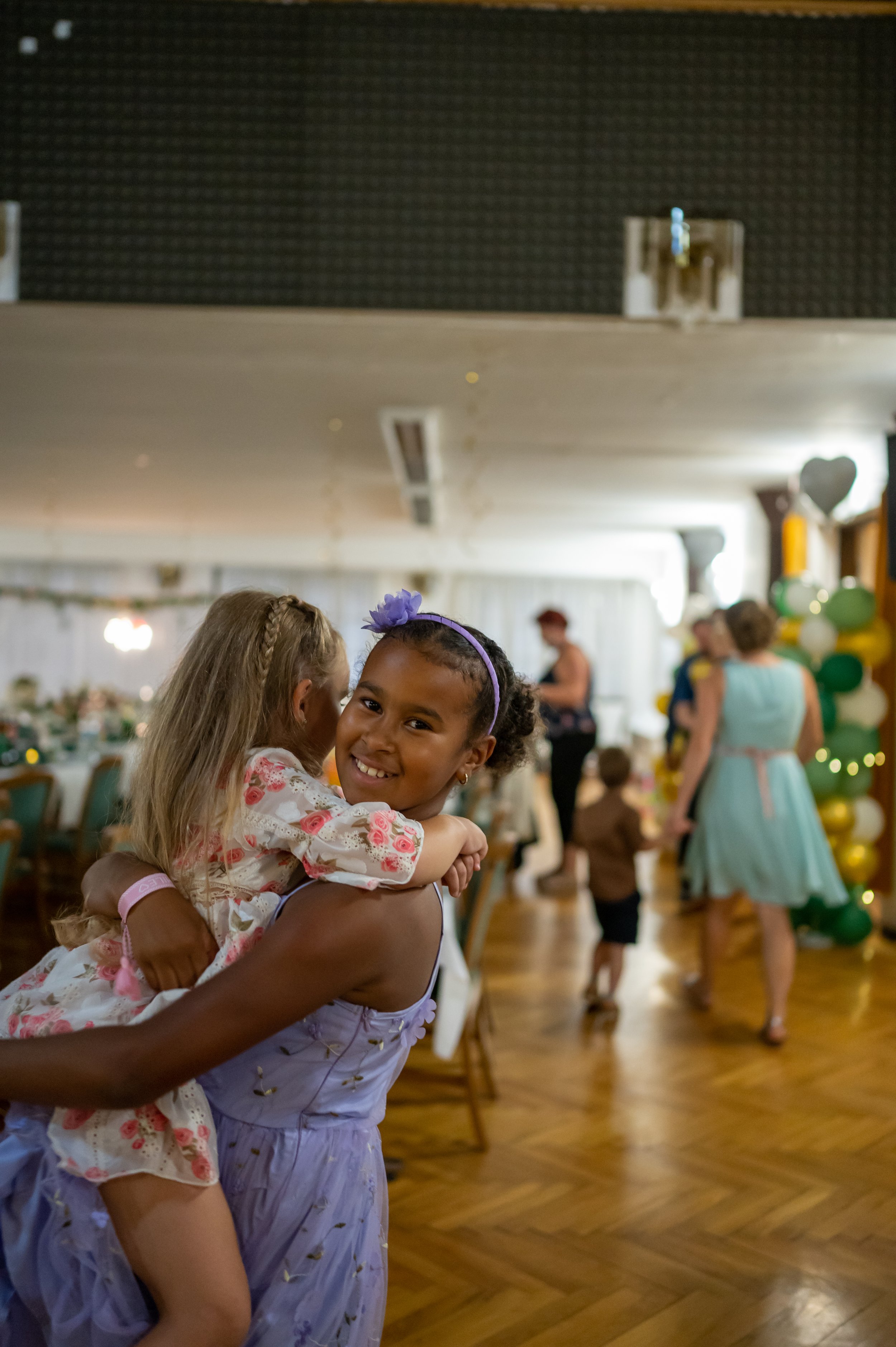 A bride is looking at her reflection in a mirror, smiling while wearing a wedding dress, in a cozy room with a window, curtains, and a swan-shaped decorative item on the windowsill.