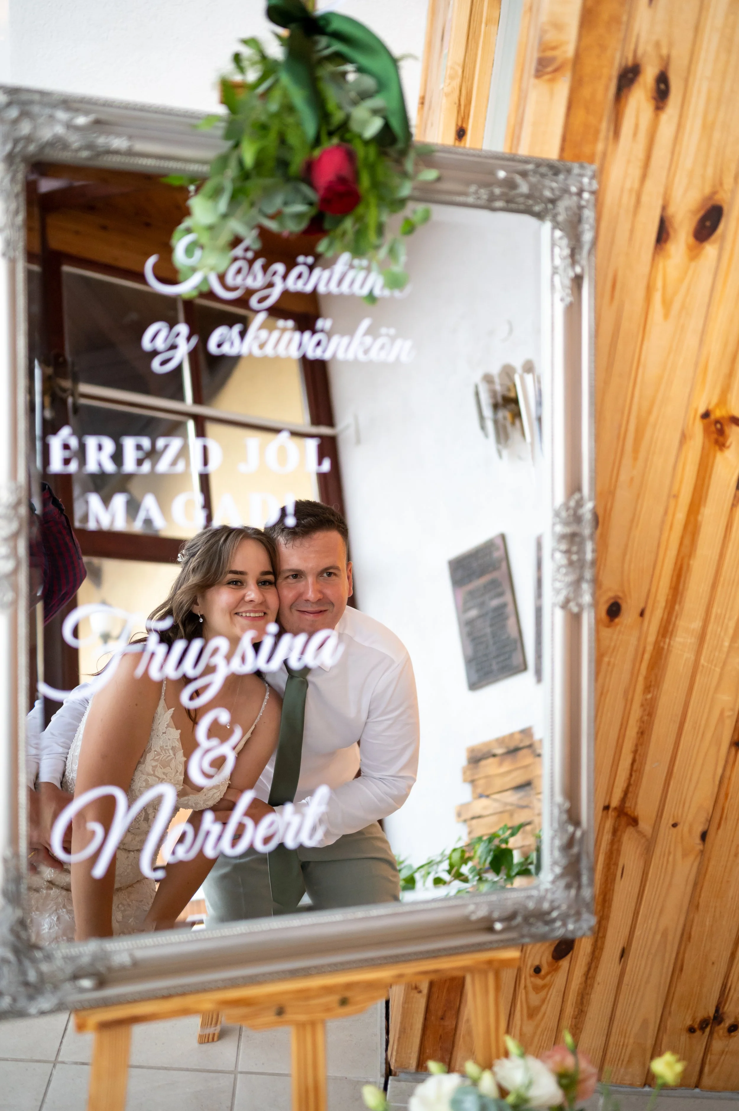 A woman in a wedding dress is seen in her reflection, putting on earrings while looking into a mirror.