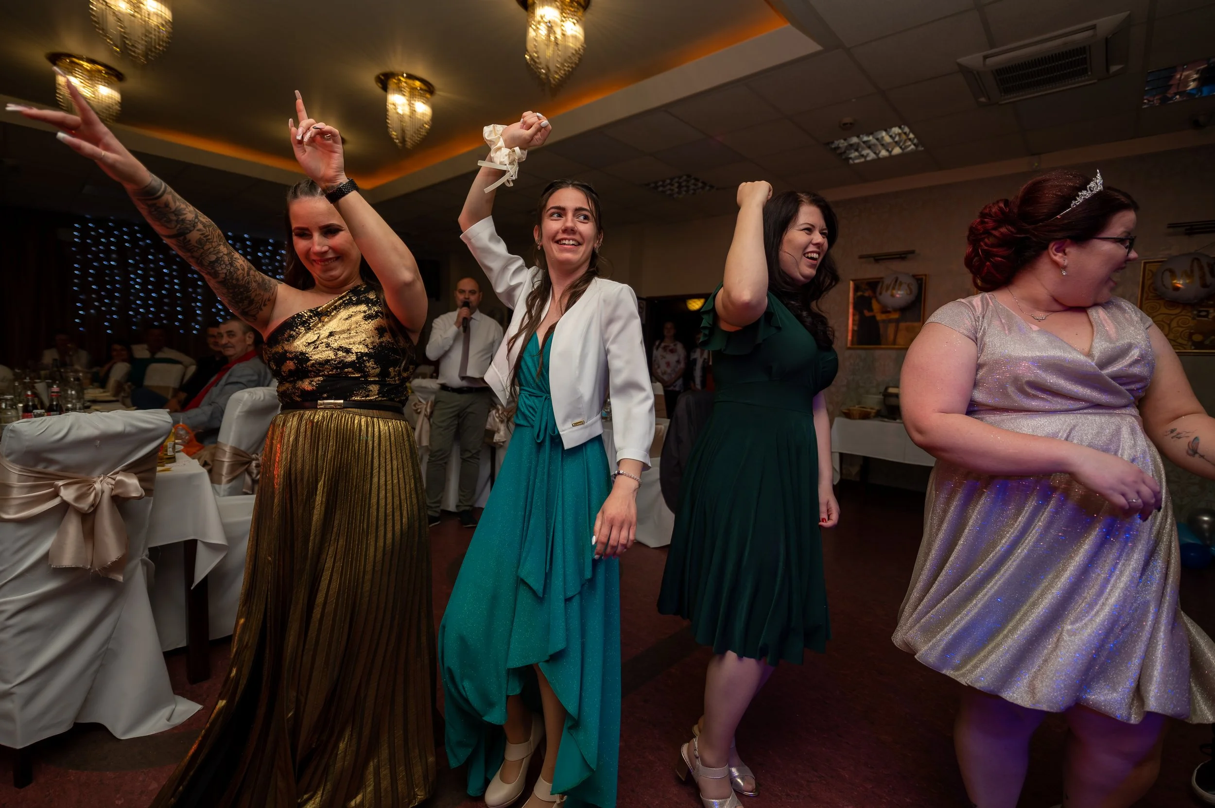 A young man in a suit getting dressed by an older woman, possibly his grandmother, in a room with wooden furniture and a window with lace curtains.