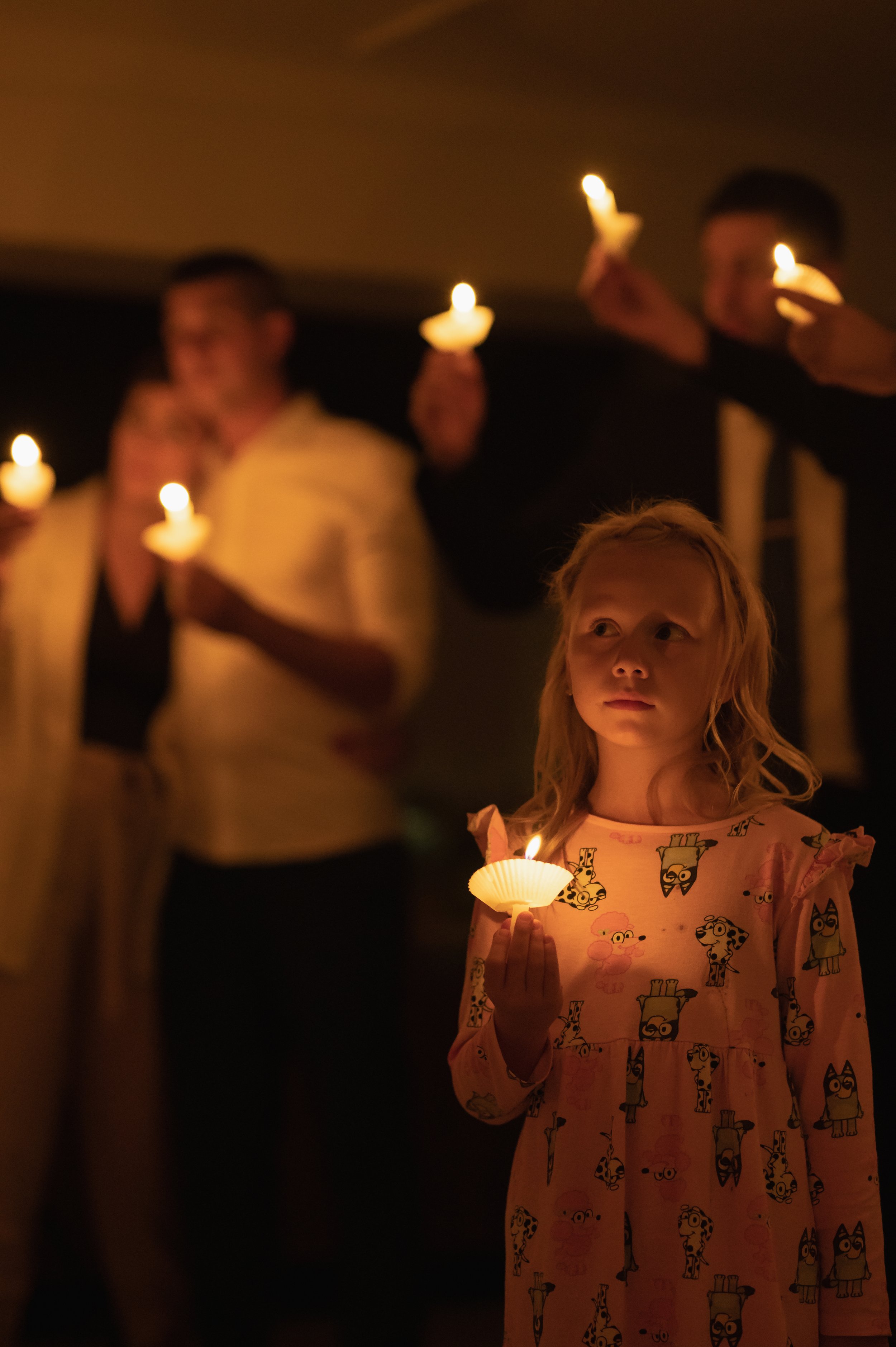 A man dressed in a white shirt and black bow tie, adjusting his watch, with a blurred background of lights.