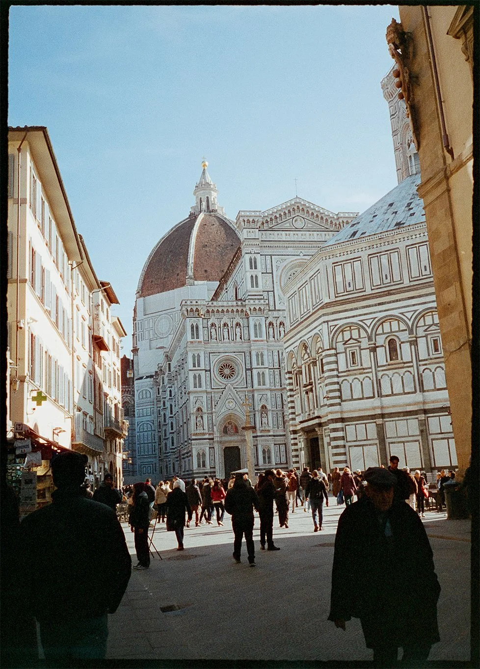 Fine art print of people walking near the Cathedral of Santa Maria del Fiore in Florence, Italy, with its distinctive dome and ornate façade visible against a clear blue sky on 35mm film Pentax 17