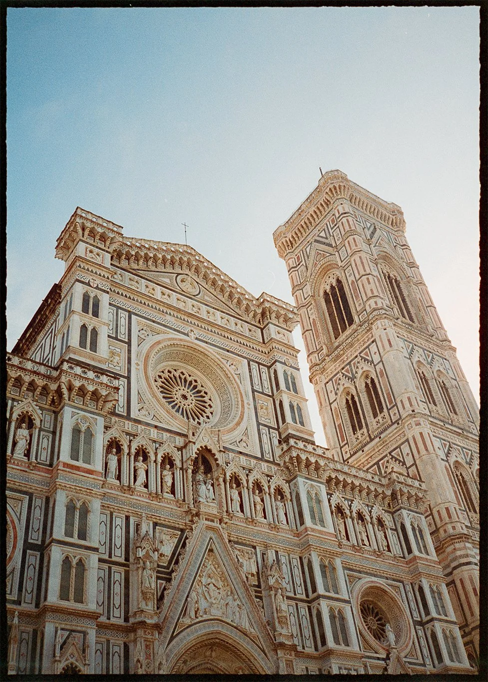 Close-up of the intricate facade and tower of Florence Cathedral in Italy, showcasing detailed marble carvings and Gothic architecture against a clear sky on 35mm film Pentax 17