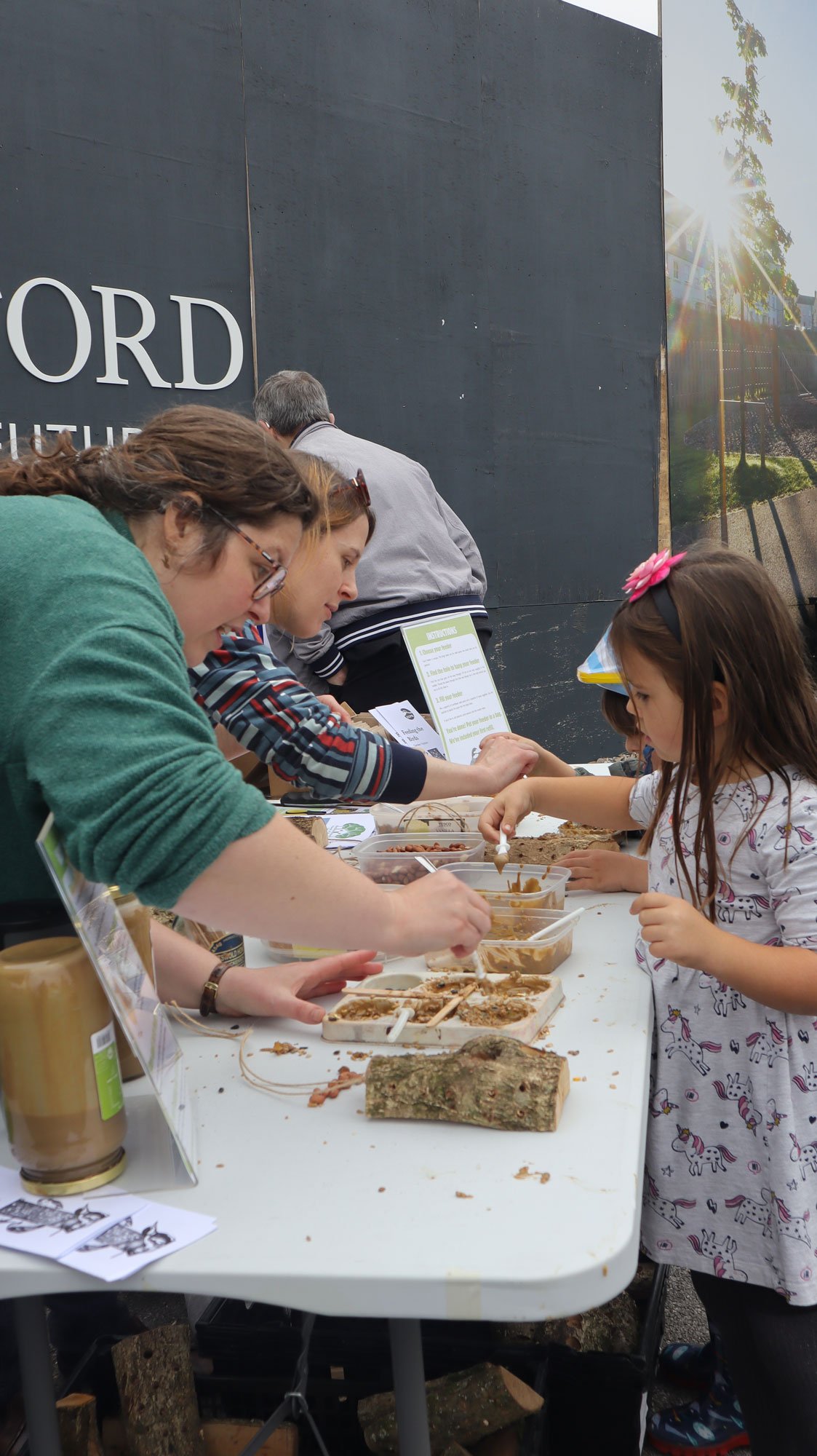 People participating in a hands-on activity at an outdoor event, with a girl engaging with a crafts or food project on a table.