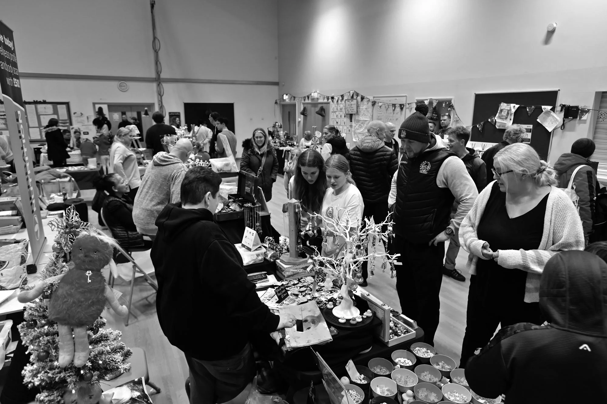 People shopping at a Christmas craft fair, browsing jewelry and holiday decorations displayed on tables.