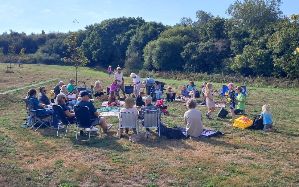 A group of adults and children gathered together, sat on chairs and on the ground, talking and playing.