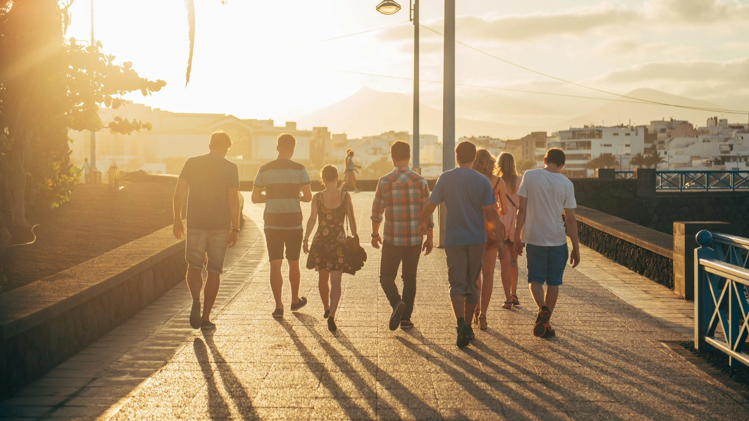 A group of people walking along a sunlit pathway at sunset in an urban area.
