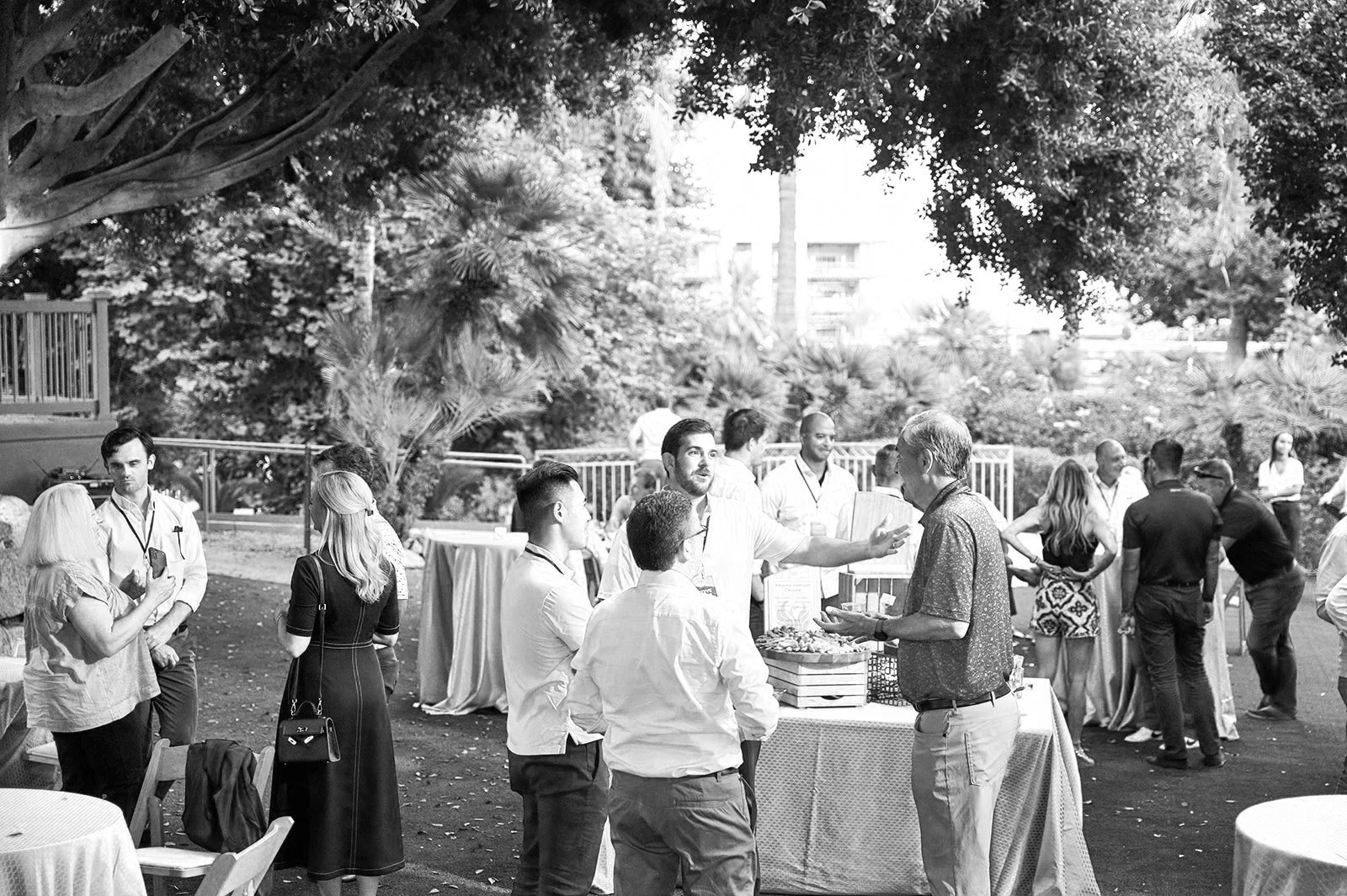 People socializing at an outdoor event with trees and buildings in the background.