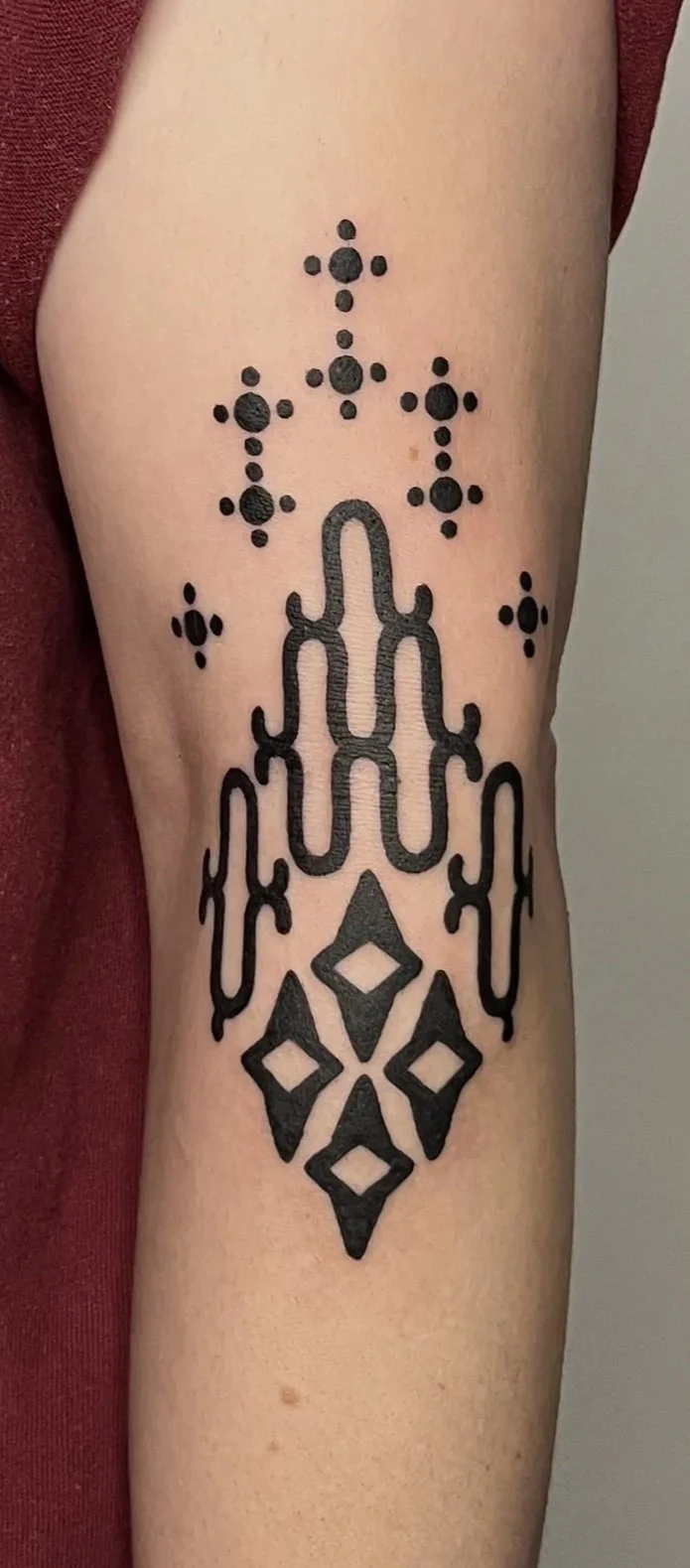 Tattoo of a black geometric chandelier design on person's forearm, above the wrist, with small dot and star-like accents.