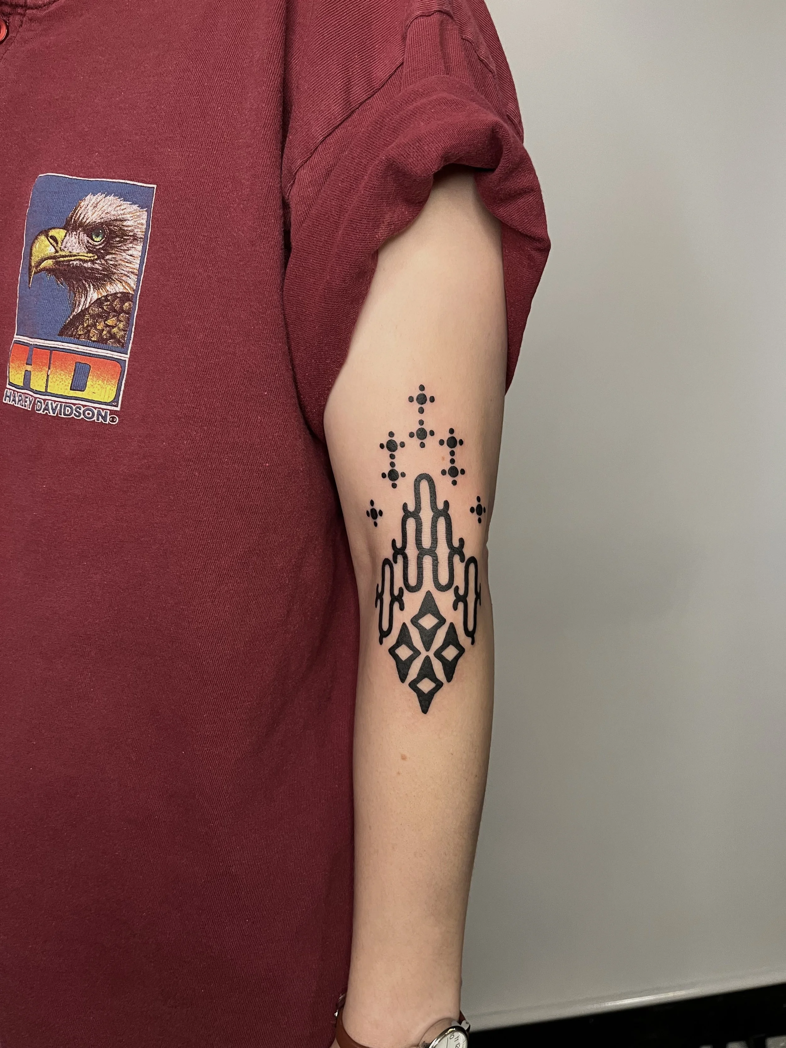 Tattoo of a black geometric chandelier design on person's forearm, above the wrist, with small dot and star-like accents.