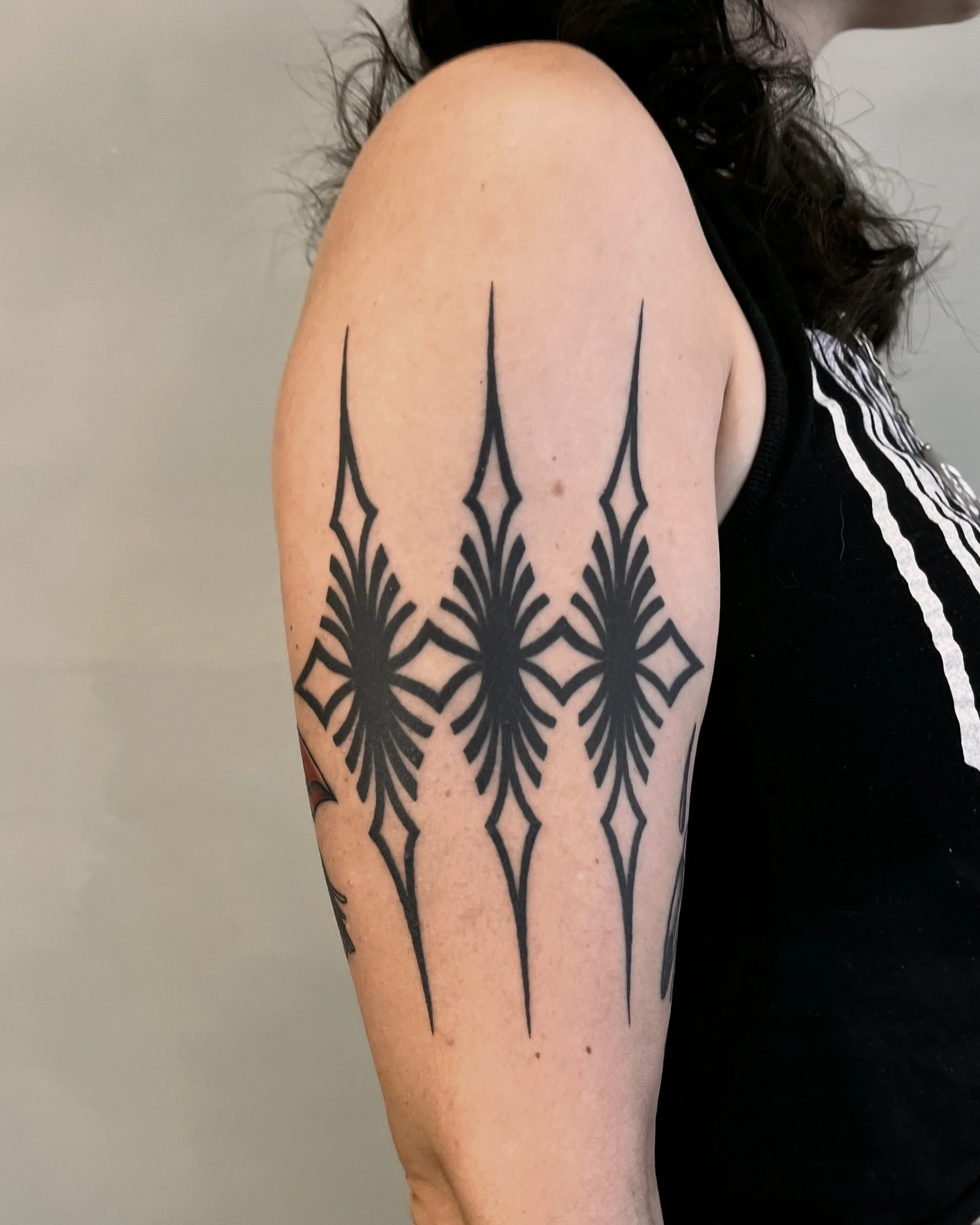 A tattoo of a geometric, tribal-inspired design on a person's upper arm, featuring black lines and symmetrical patterns.