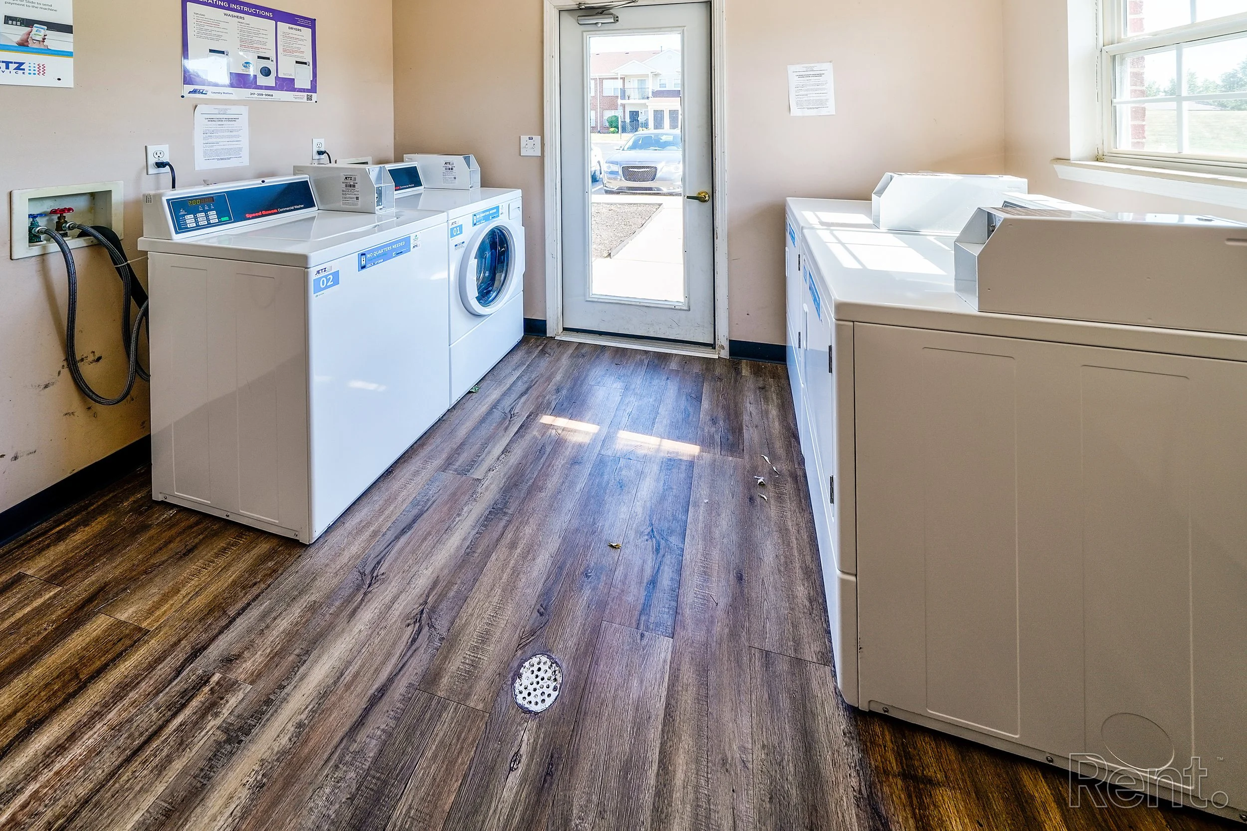 Laundry room with washing machines, wooden floor, and a door leading outside.