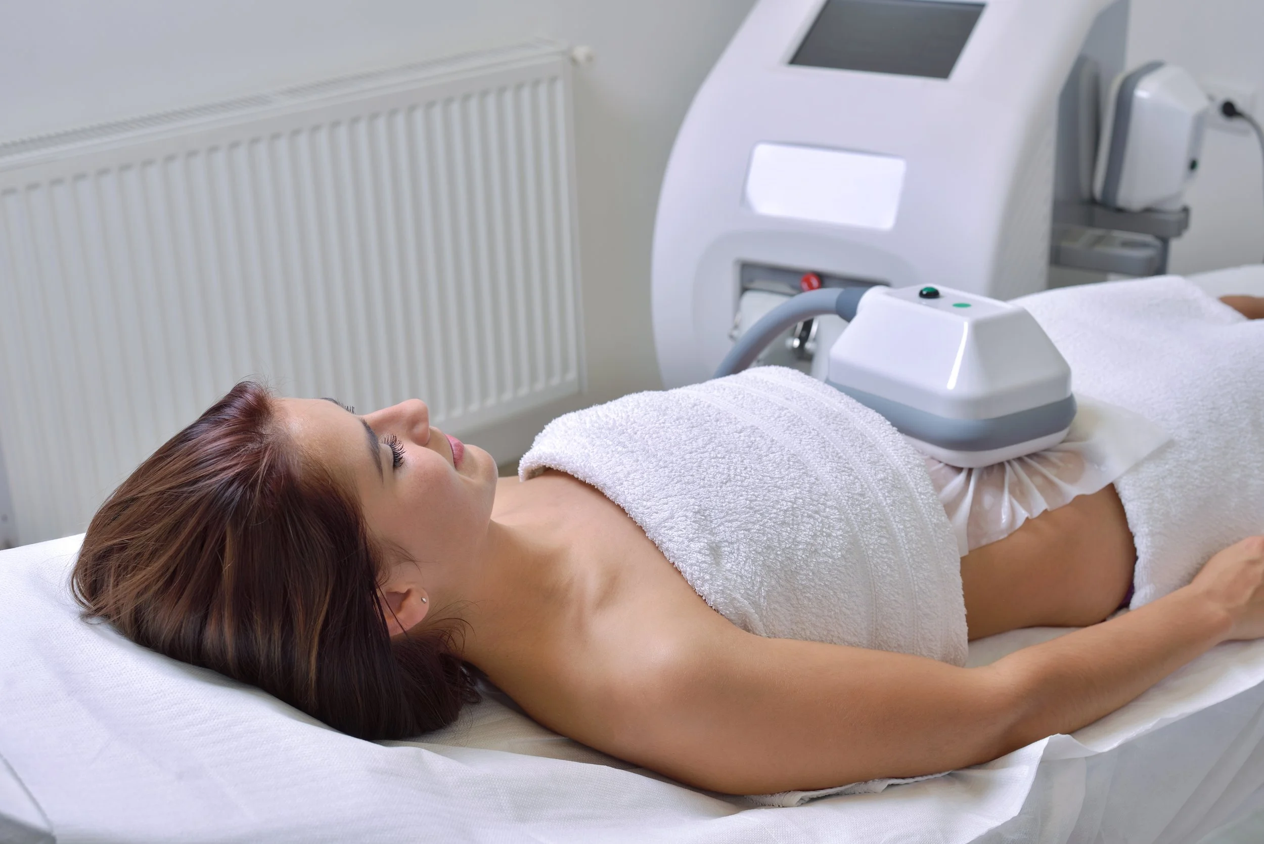 Woman receiving a non-invasive body contouring treatment with a laser or radio frequency machine at a clinic.