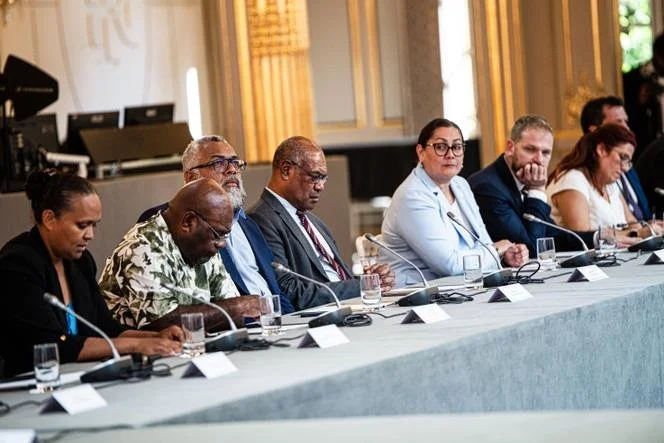 Un groupe de personnes assises à une table lors d'une réunion ou d'une conférence, avec des microphones et des verres d'eau devant elles.