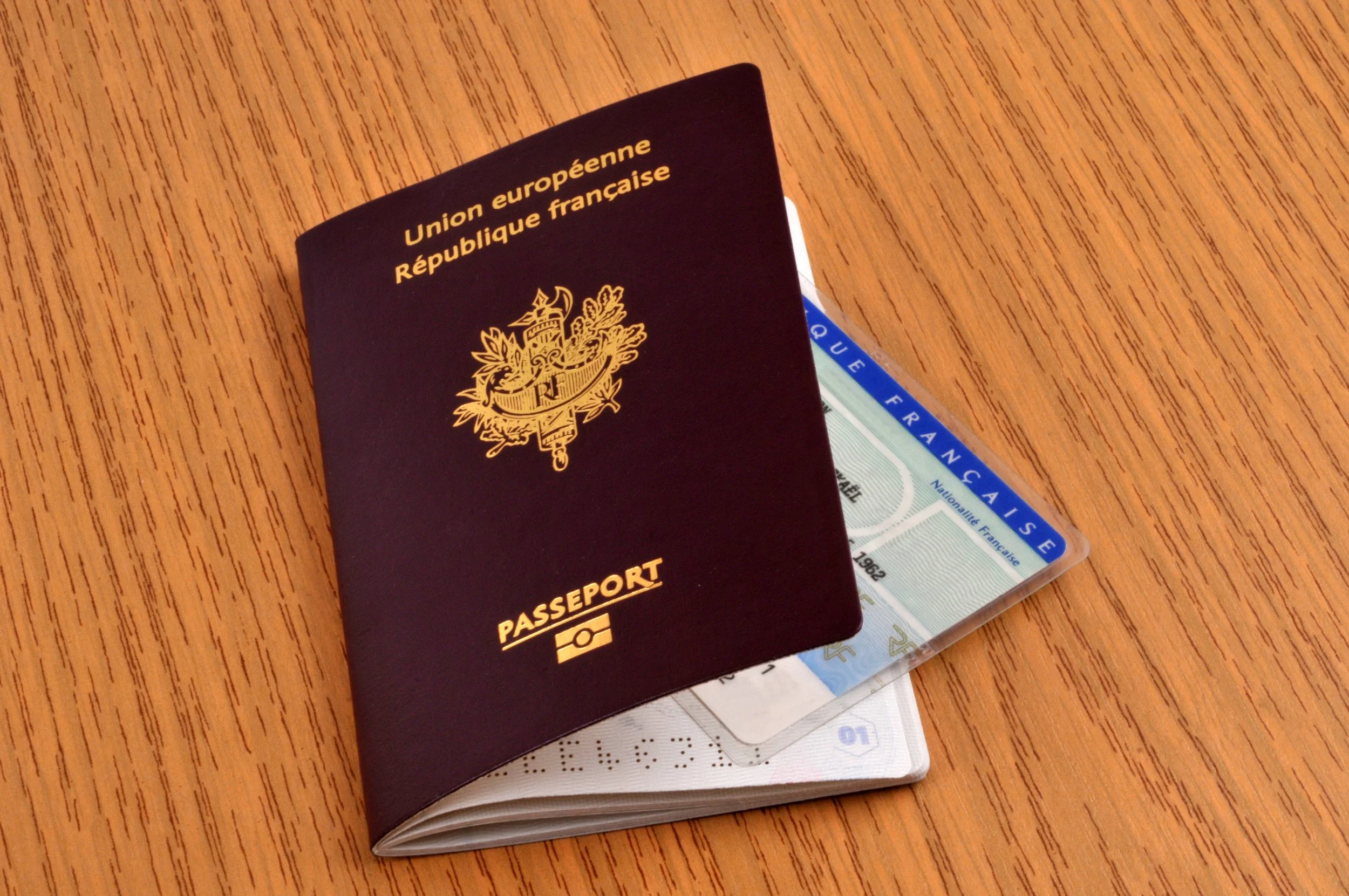 Un passeport français ouvert avec une carte d'identité à l'intérieur, posé sur une surface en bois.