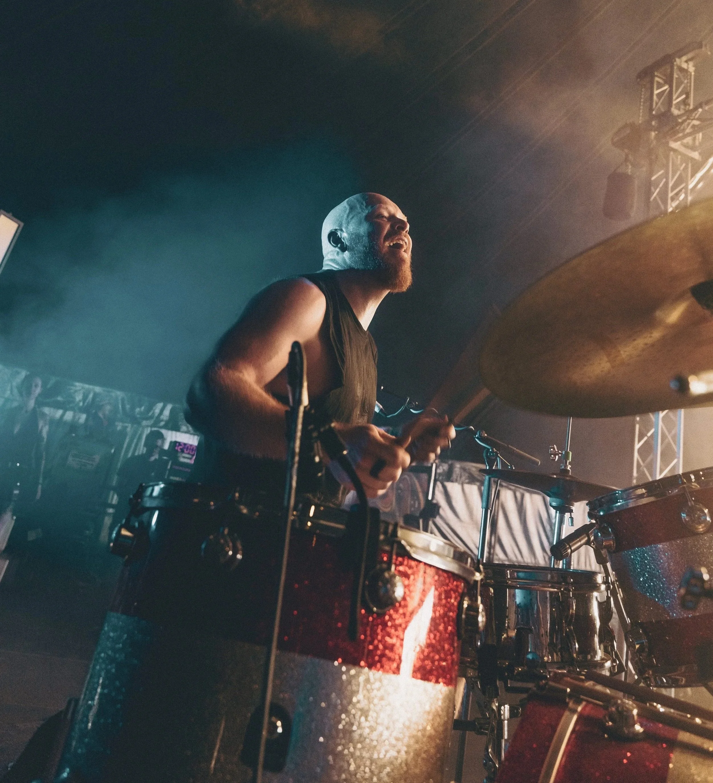 Drummer playing drums on stage with stage lights in the background.