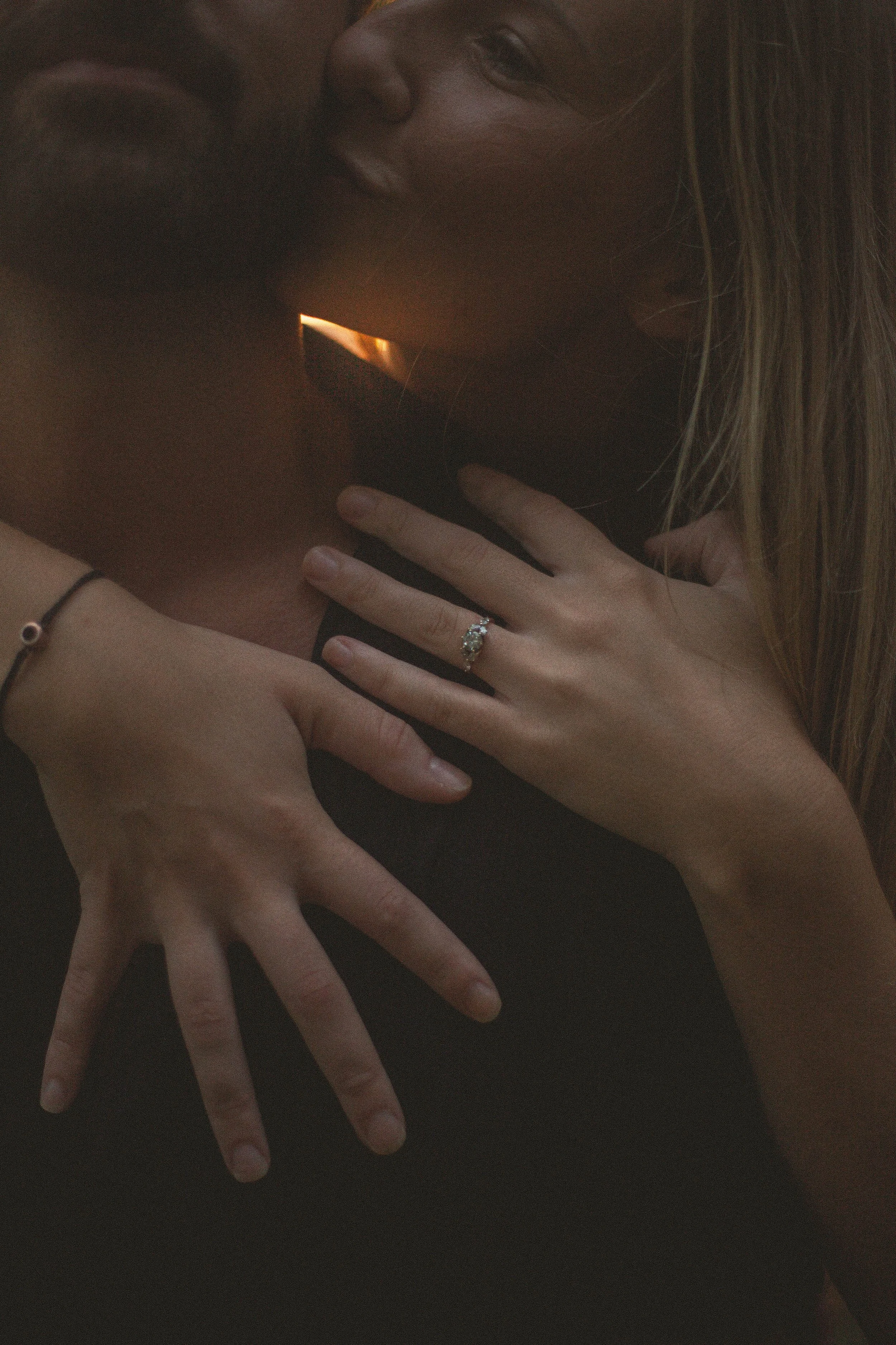 Close-up of a couple embracing, with their faces partially visible and their hands intertwined, highlighting a wedding ring on the wife's finger.