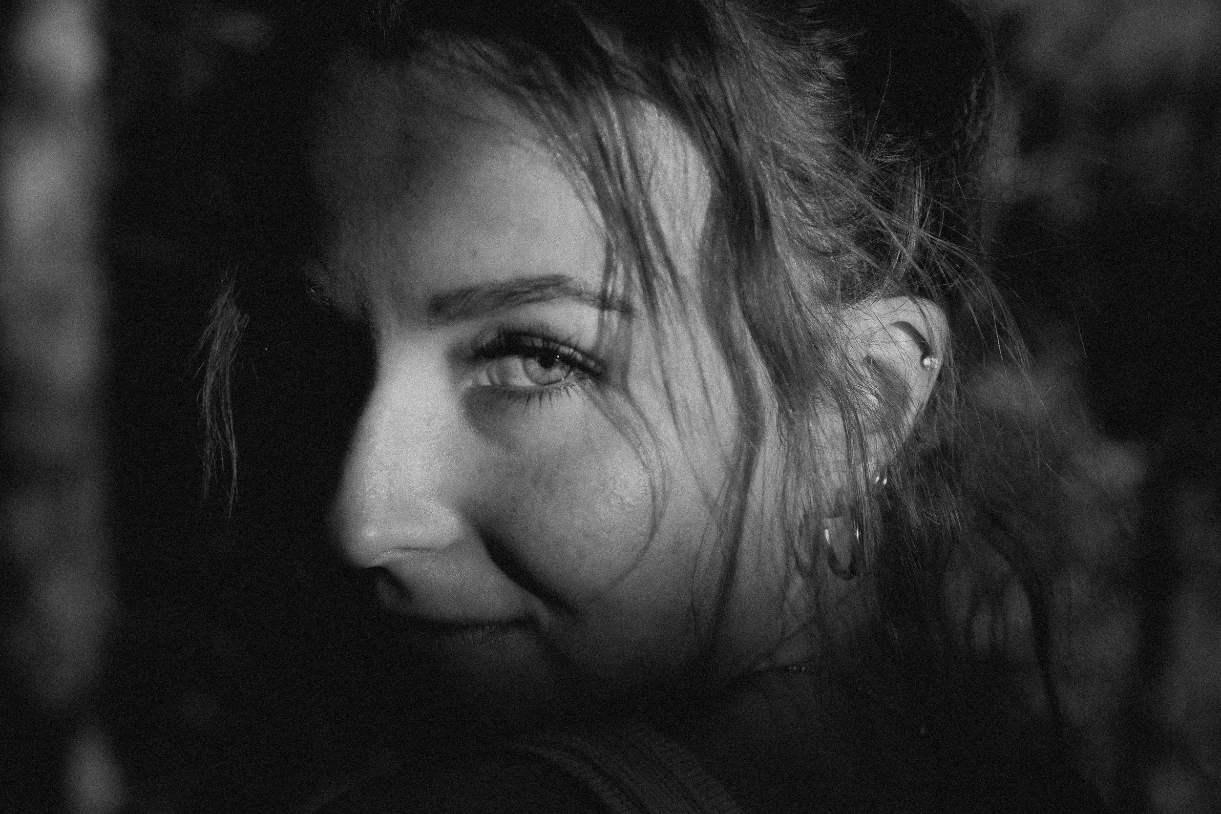 Close-up black and white photo of a young woman with light-colored eyes, smiling, with her face turned slightly to the side and her hair falling across her forehead.