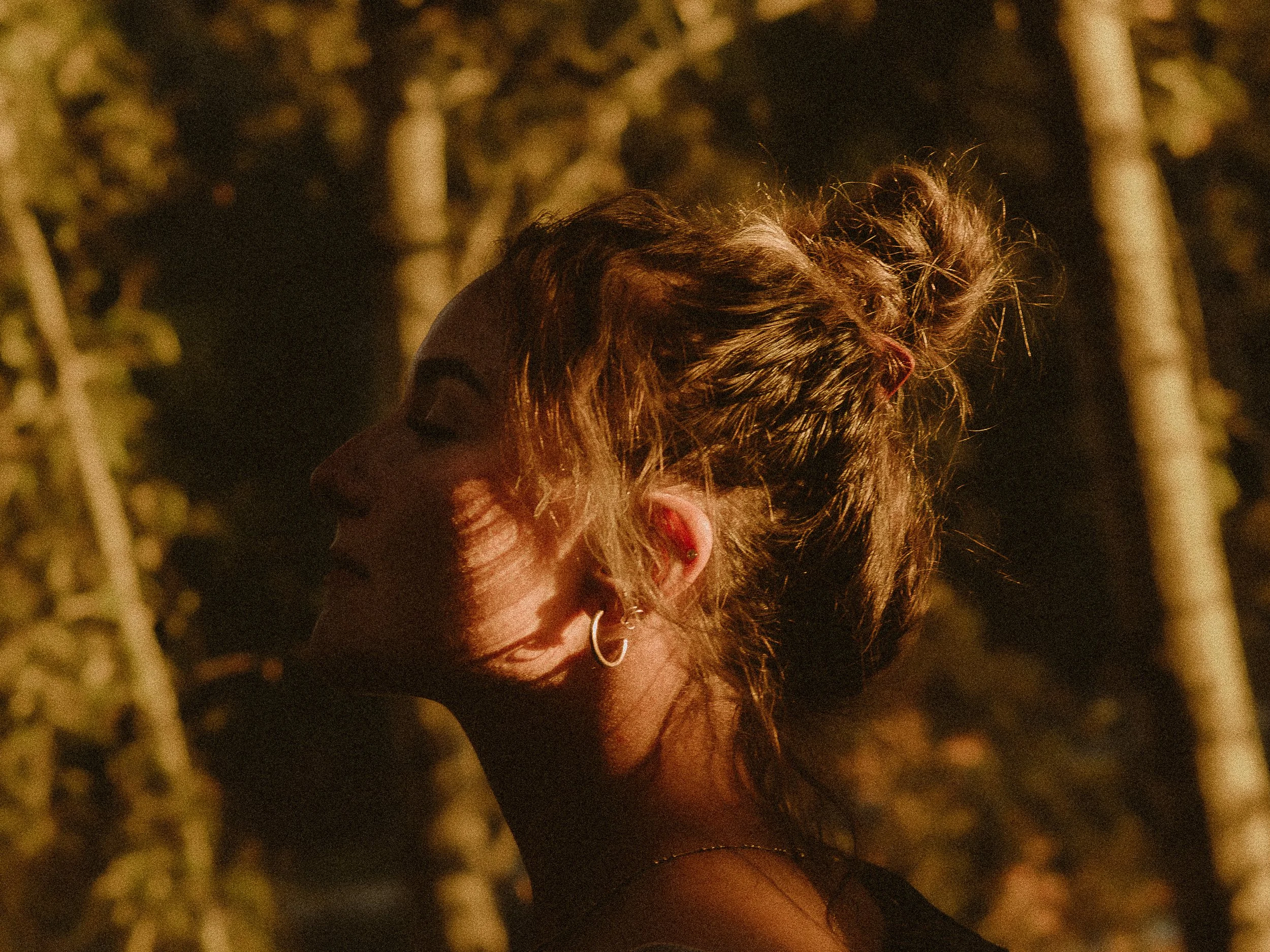 Profile of a woman with her eyes closed, illuminated by golden sunlight, with trees in the background.