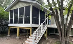 A three-season porch addition with a screened-in porch being built on stilts, and a staircase leading up to the porch, surrounded by trees.