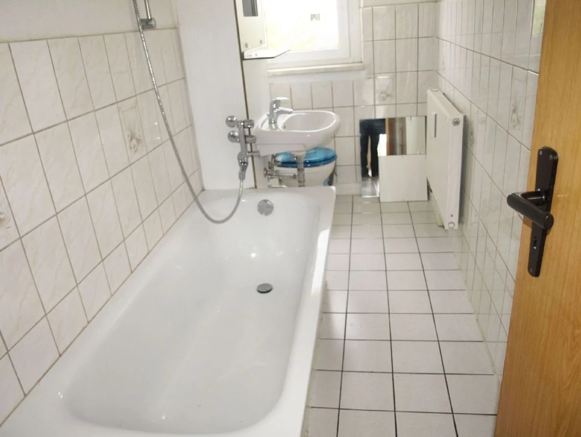 Salle de bain avec baignoire, lavabo, miroir, radiateur et porte en bois, vue depuis l'entrée