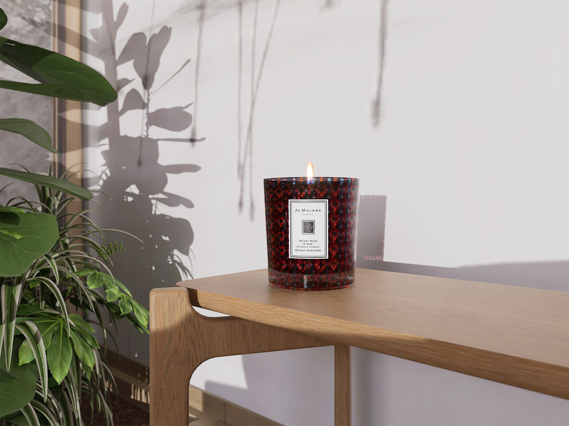 Bougie rouge dans un vase en verre sur une table en bois, avec une plante verte à gauche et une ombre portée de la plante sur le mur blanc derrière.