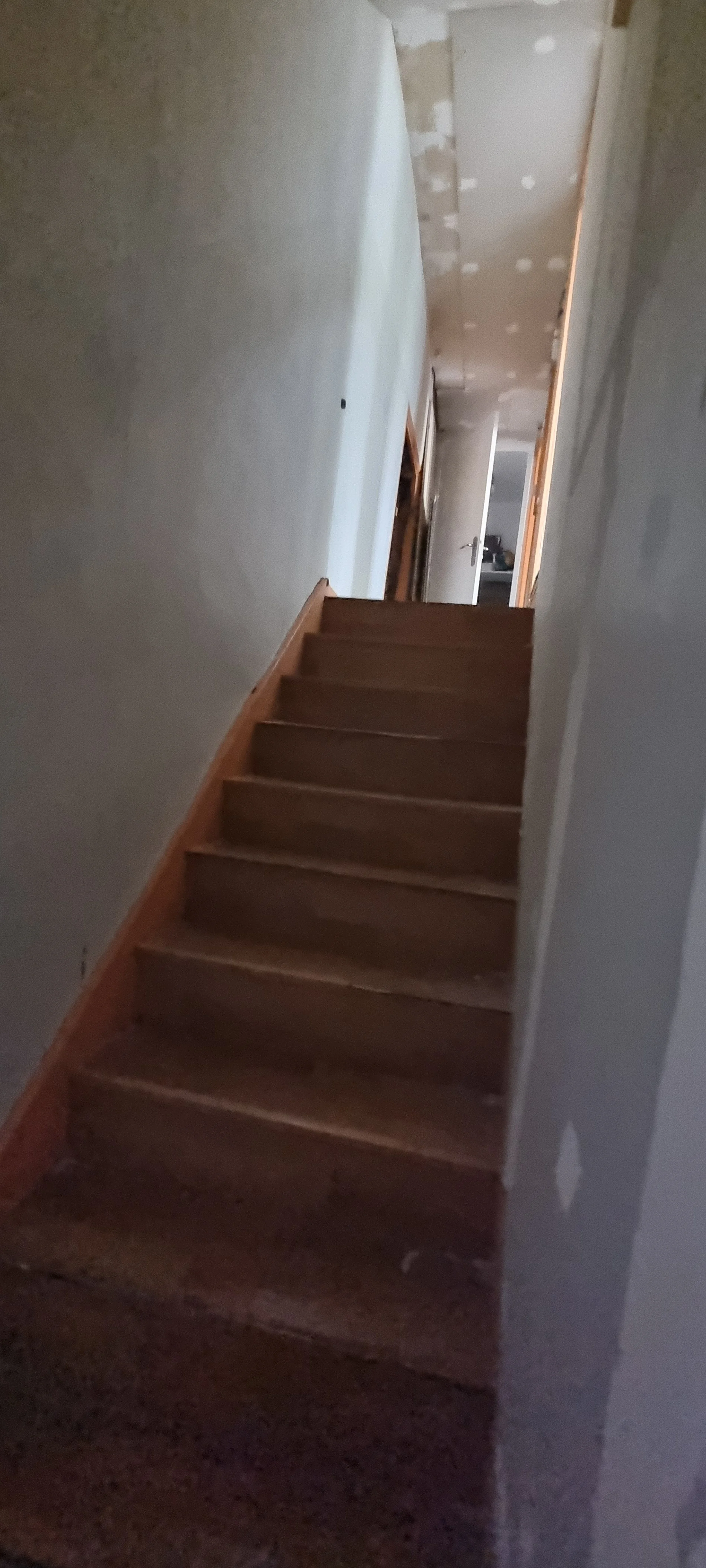 Escalier en bois menant à un couloir dans une pièce en cours de rénovation avec des murs partiellement enduits.