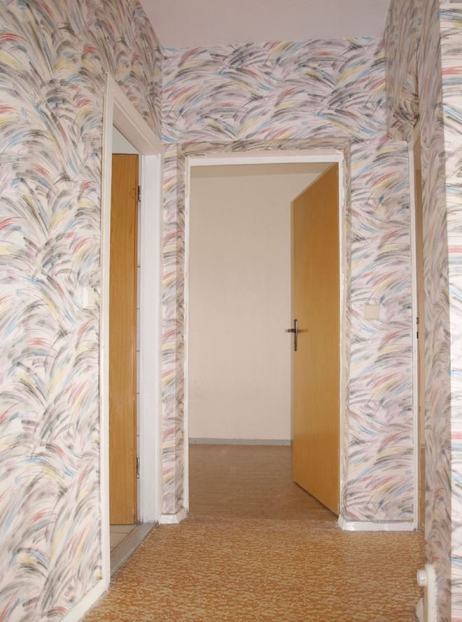 Un couloir dans une maison avec des murs décorés de papier peint coloré, trois portes en bois, et un sol en tapis beige.