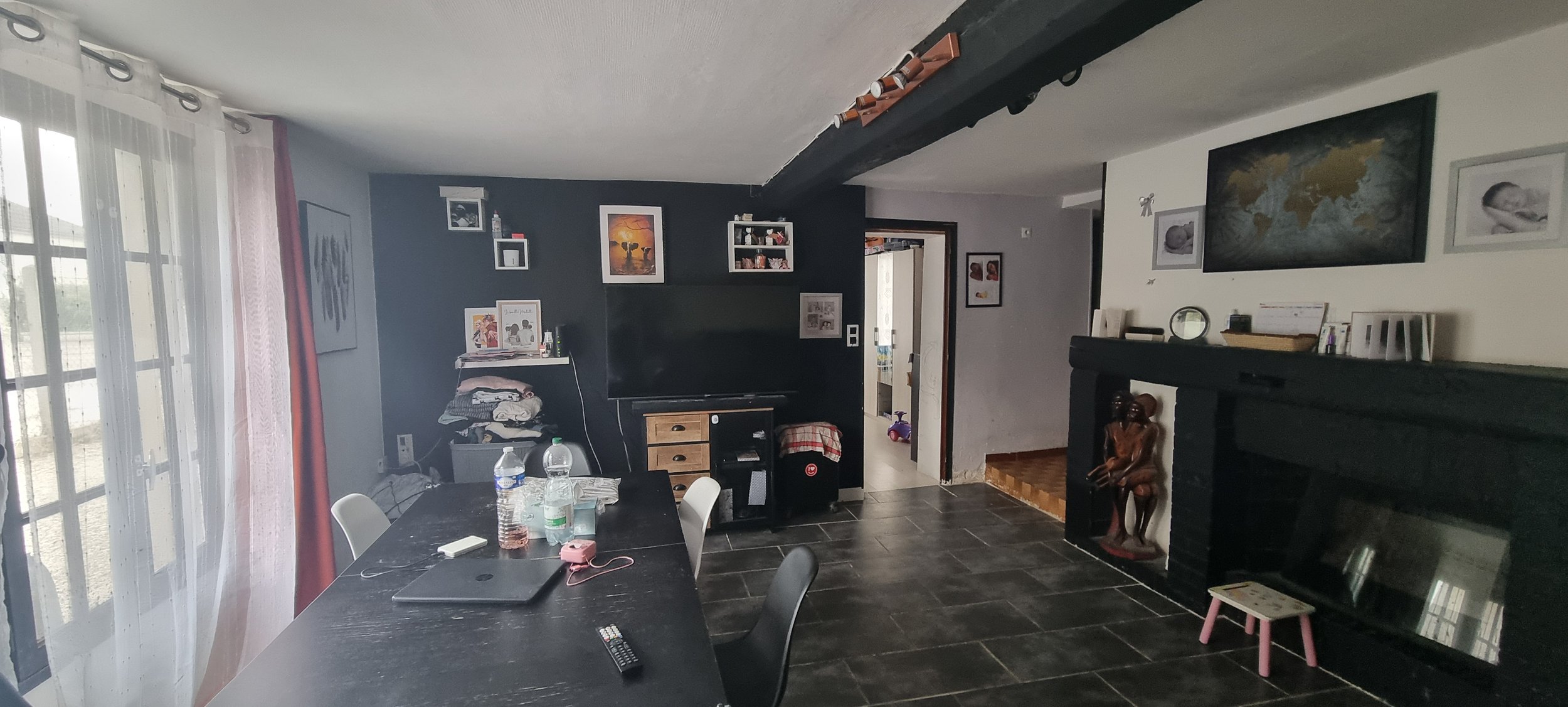 Salon avec un mur bleu foncé, une télévision, une cheminée noire, une table, des chaises, et des décorations de mur.