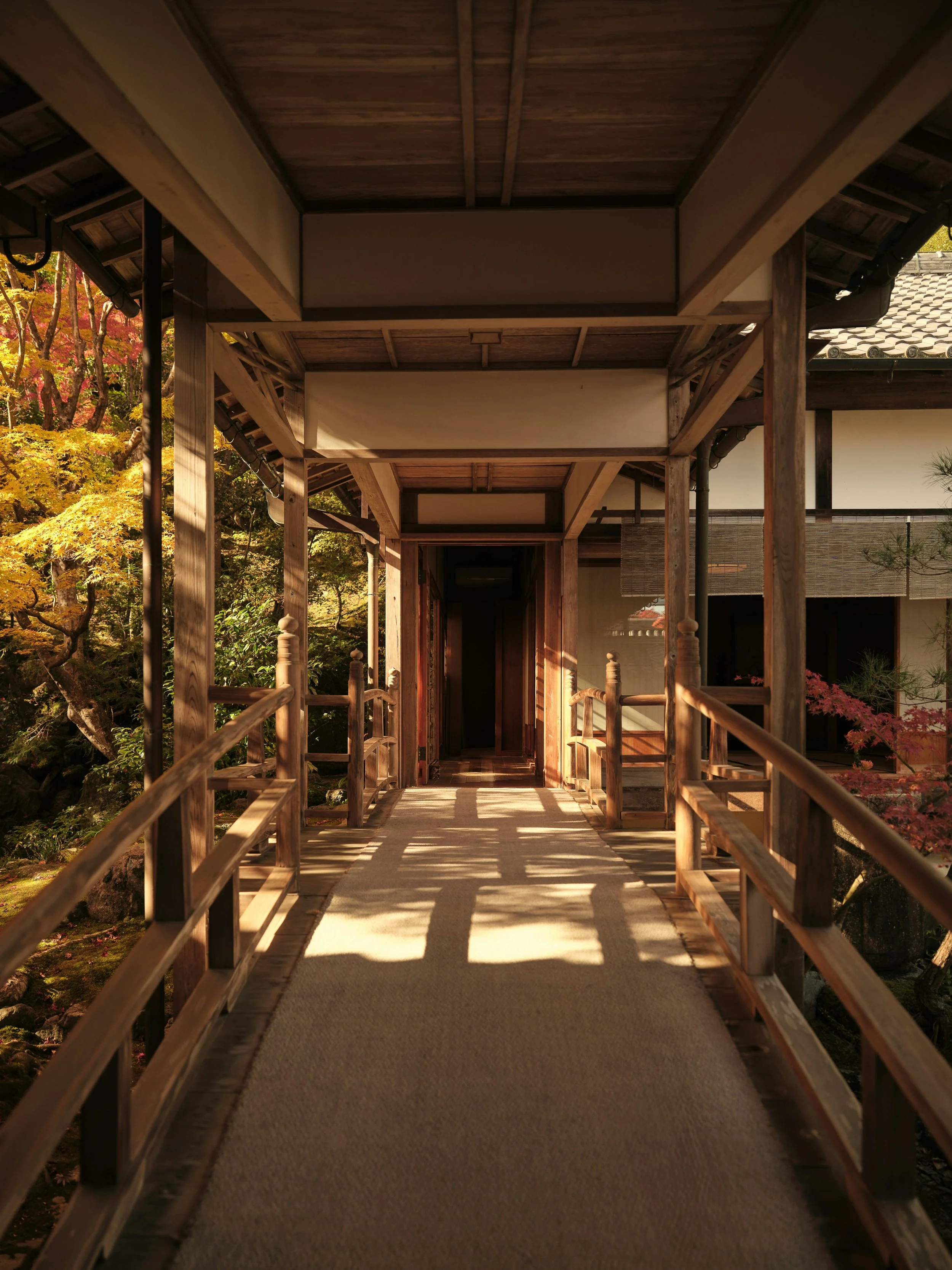 Passerelle en bois menant à une maison traditionnelle japonaise entourée d'arbres en automne.