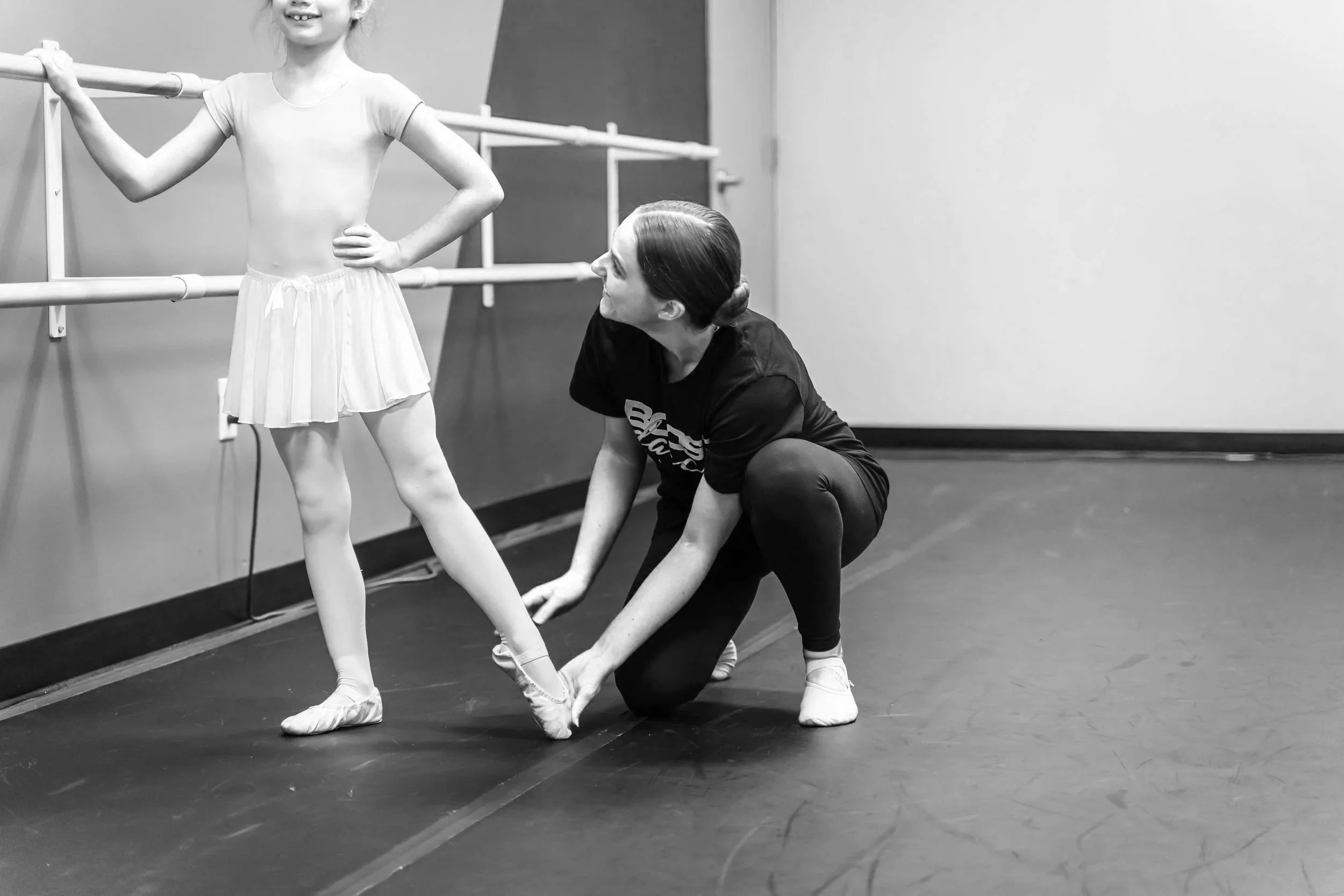 A ballet instructor helping a young girl with her ballet shoes in a dance studio.