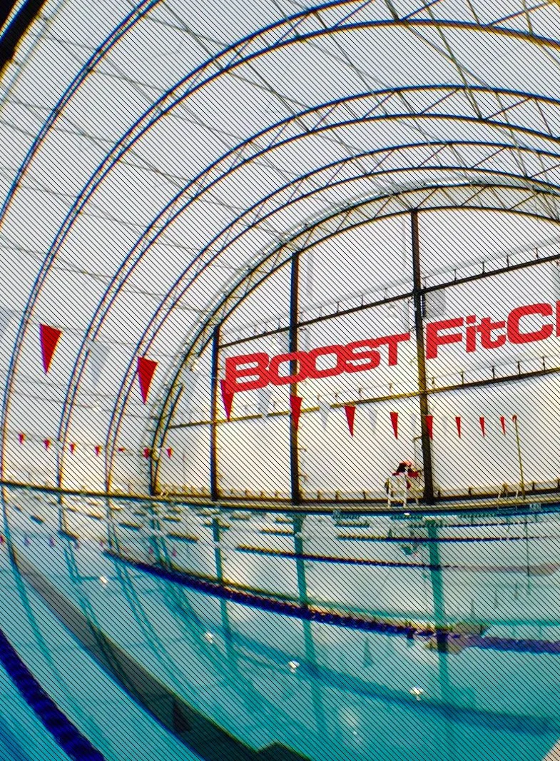 Indoor swimming pool with a large glass dome ceiling and the words 'BOOST FIT CLUB' on the window.