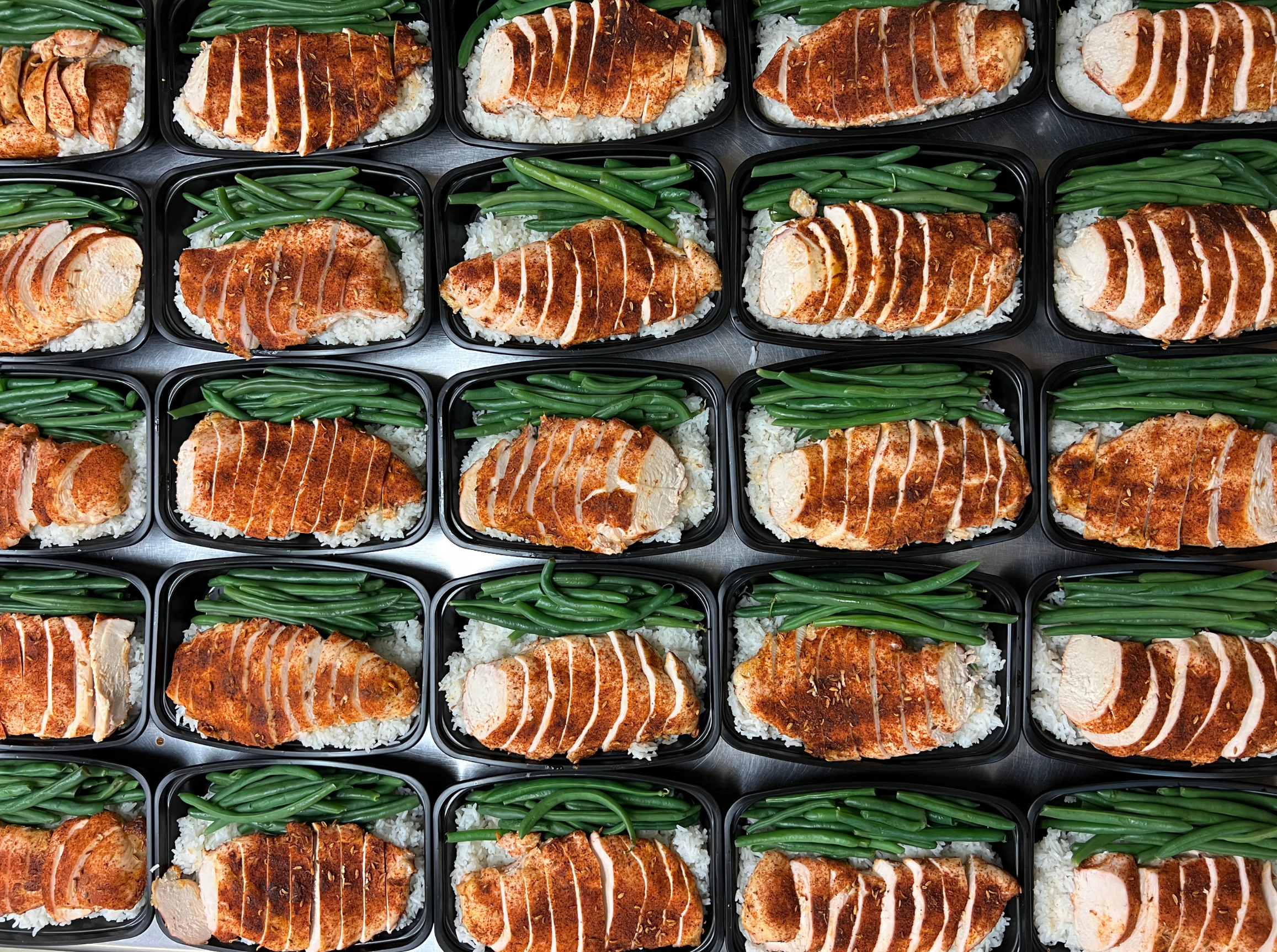 Multiple meal prep containers filled with rice, green beans, and seasoned sliced chicken breast.
