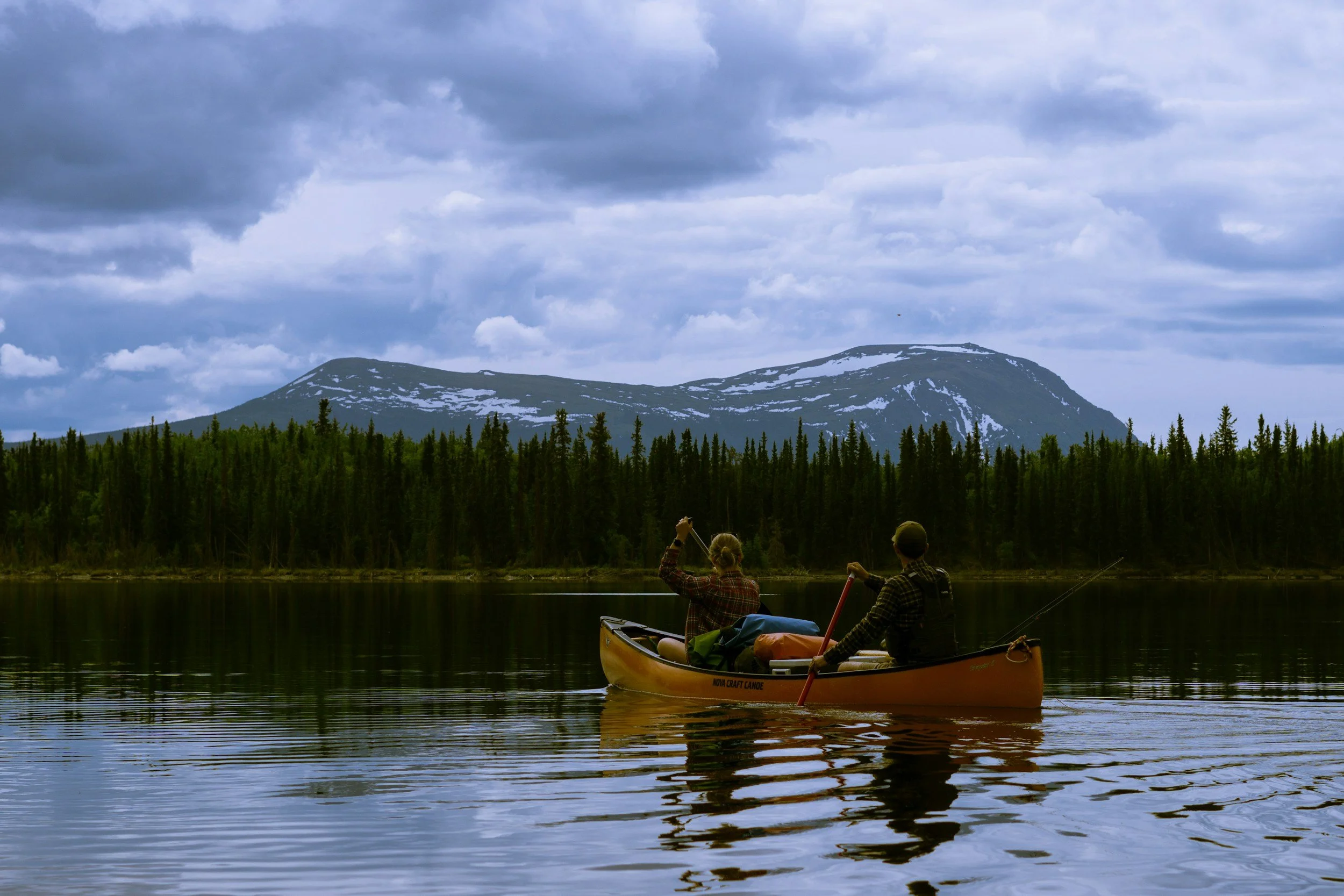 Two people paddling a canoe on a Yukon lake with mountain backdrop, symbolizing mortgage renewals and Northern lifestyle goals.