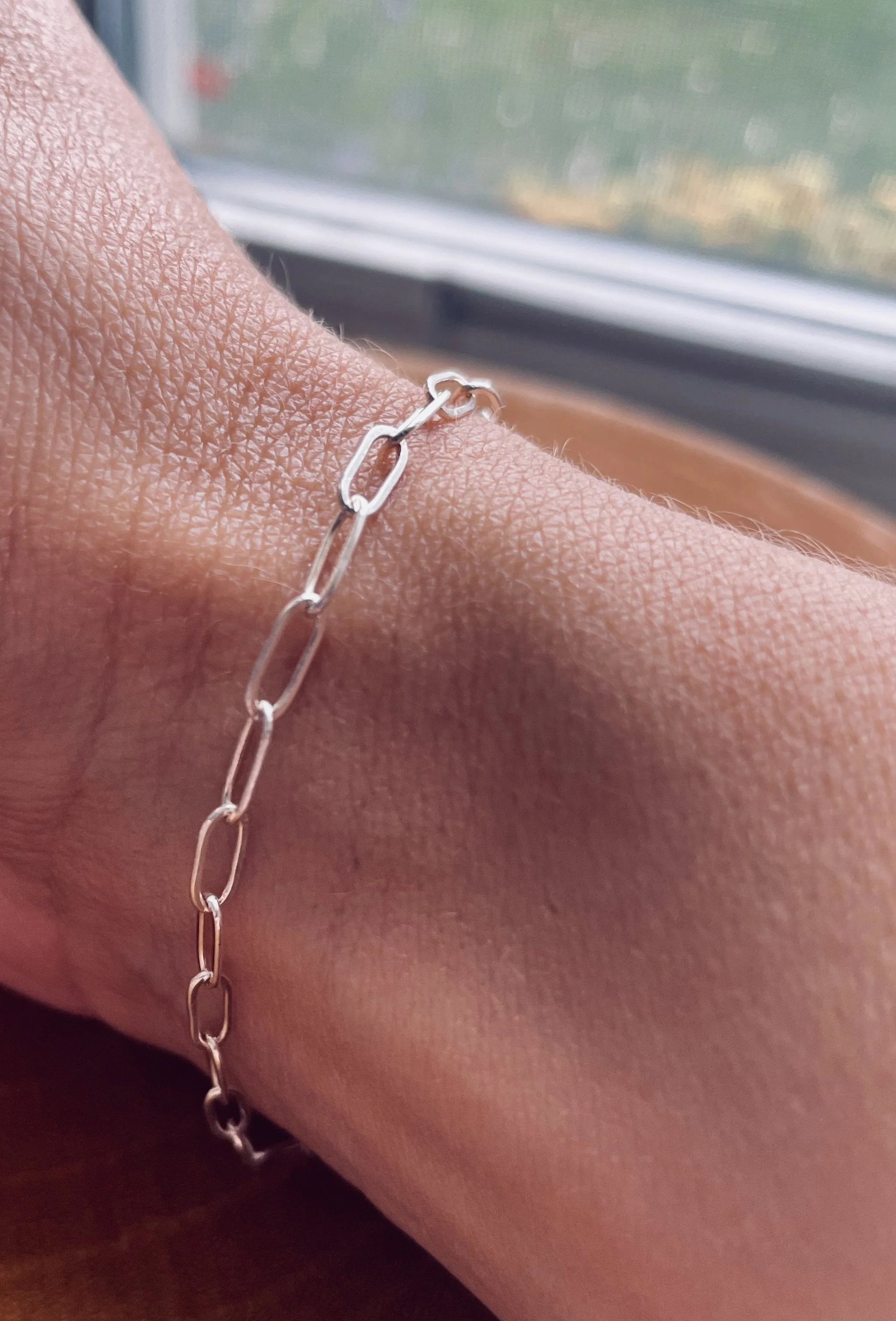 Close-up of a silver chain bracelet on a person's wrist near a window.