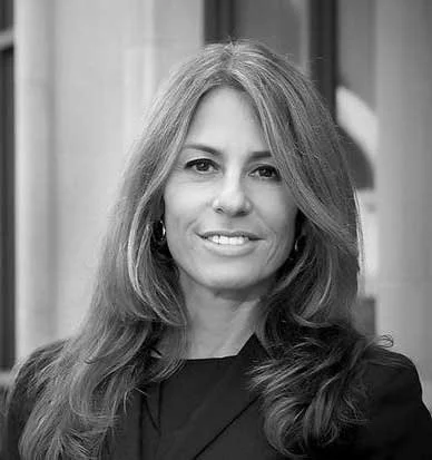 Black-and-white portrait of a woman with long, wavy hair smiling at the camera.