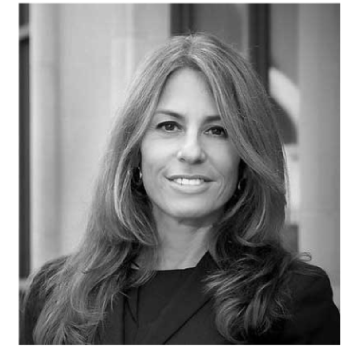 Black and white portrait of a woman with long, wavy hair, smiling, wearing earrings and a dark blazer.