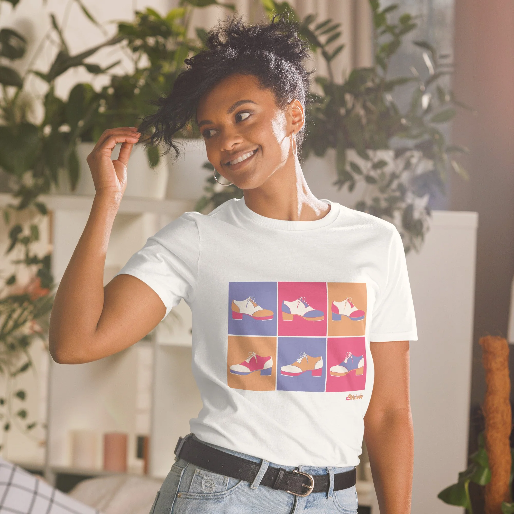 A woman in her 20s, brown skin and hair wearing a white graphic tee with tap shoes on it in a pop art style.