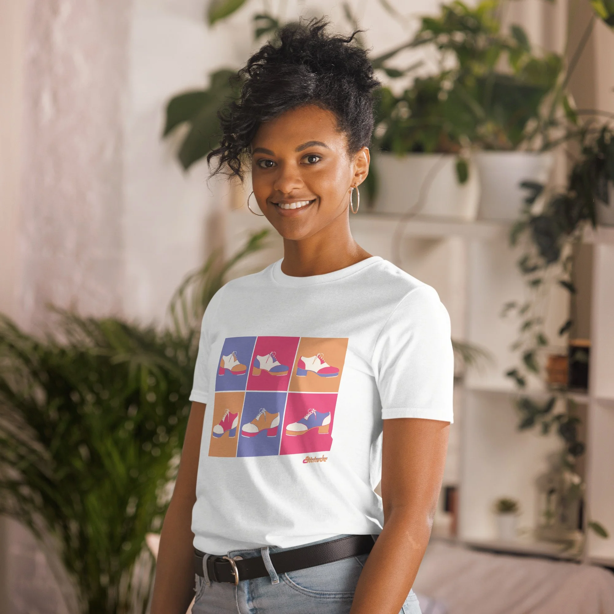 A woman in her 20s, brown skin and hair wearing a white graphic tee with tap shoes on it in a pop art style.