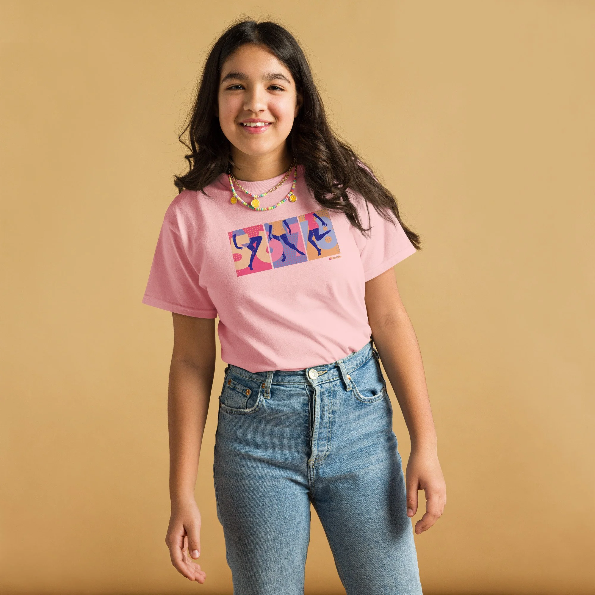 A teen girl with brown hair wearing a pink graphic tee with 5,6,7,8 and three dancers' legs spanning 3 panels, blue jeans.