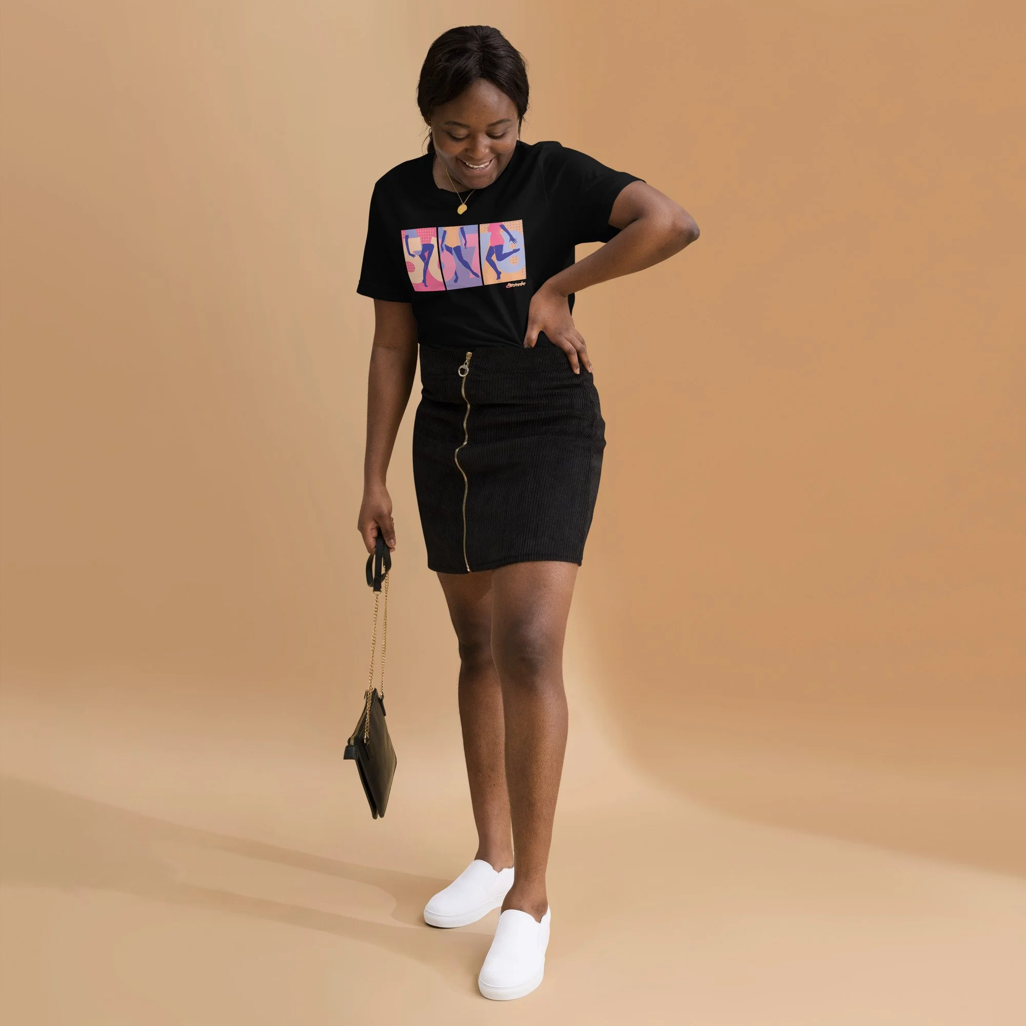 A black woman in her 20s wearing a black graphic tee with 5,6,7,8 and a dancer in three panels, a demin skirt, and white shoes.
