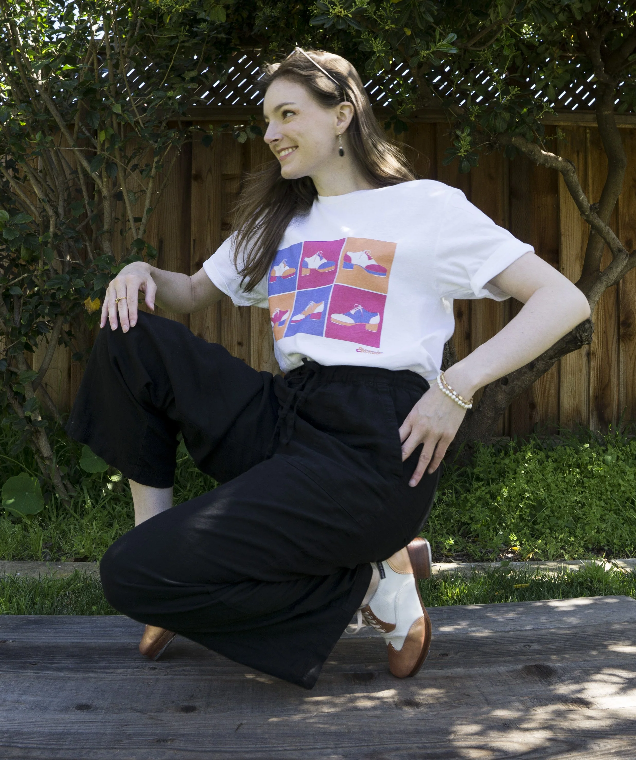 Miss Alex outside on her tap board wearing tap shoes and a white graphic tee with Pop art inspired tap shoe design.