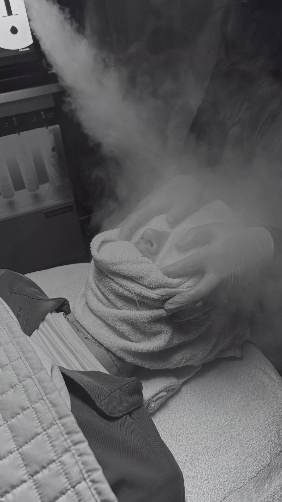 A person lying in a treatment bed receiving a steam treatment prior to a signature hydrafacial by valerie