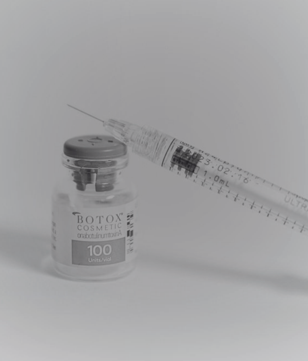 A vial labeled Botox cosmetic next to a syringe on a white surface.