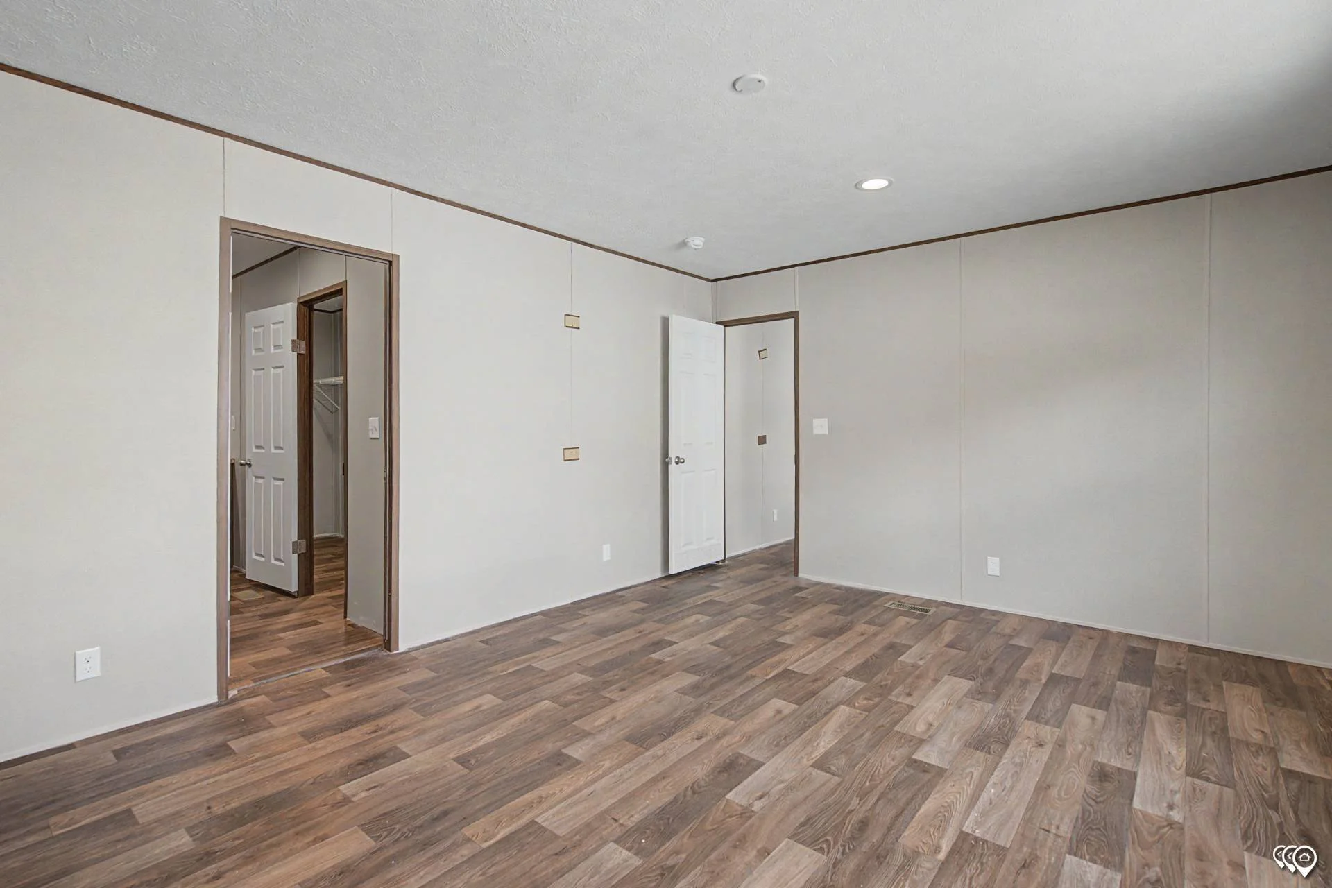 An empty room with white walls, wood flooring, and three open doors revealing closets and another room.