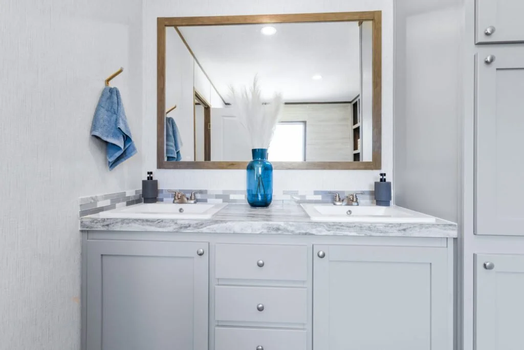 Bathroom double vanity with a marble countertop, mirrors, and a blue vase with white pampas grass, with blue towels on the wall.