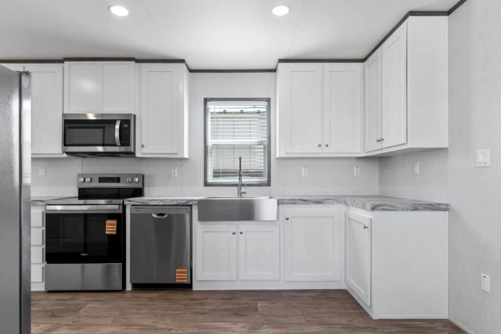 Modern kitchen with white cabinets, stainless steel appliances including oven, microwave, refrigerator, and dishwasher, gray marble countertops, and a window above the sink.