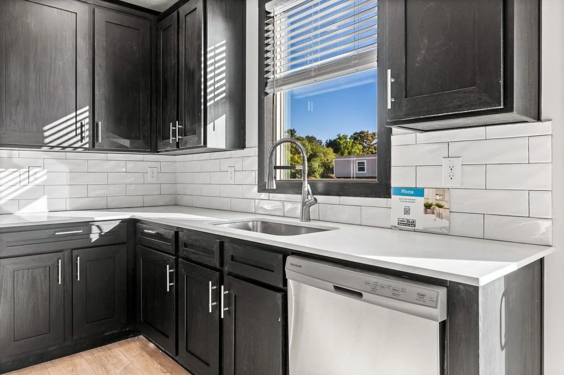 Modern kitchen with dark cabinets, white countertop, white subway tile backsplash, stainless steel faucet, window with blinds, and dishwasher.