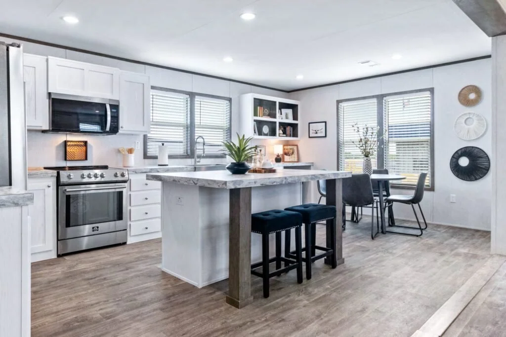 Modern kitchen with white cabinetry, stainless steel appliances, black chairs around a dining table, and decorative wall art.